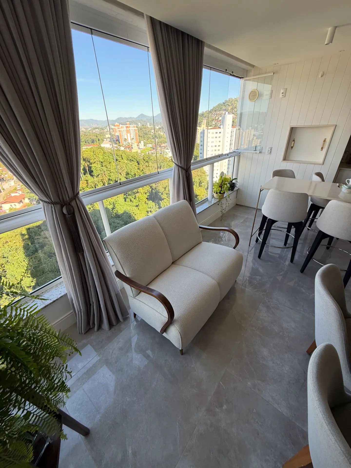 Poltrona de dois lugares estofada em bouclé creme em varanda com vista para Blumenau